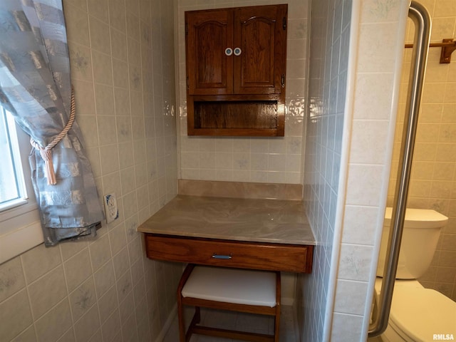 bathroom with toilet, tile walls, and a shower with shower door