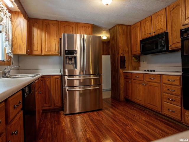 kitchen with a textured ceiling, black appliances, sink, and dark hardwood / wood-style floors