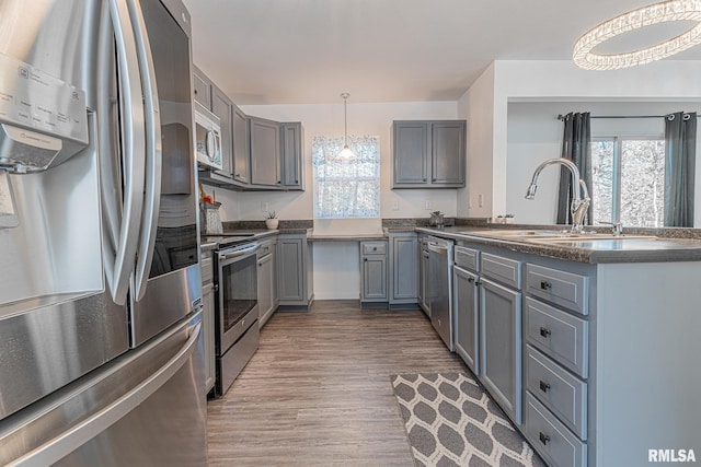 kitchen with decorative light fixtures, wood-type flooring, gray cabinetry, and stainless steel appliances