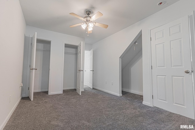 unfurnished bedroom with ceiling fan, two closets, and dark colored carpet