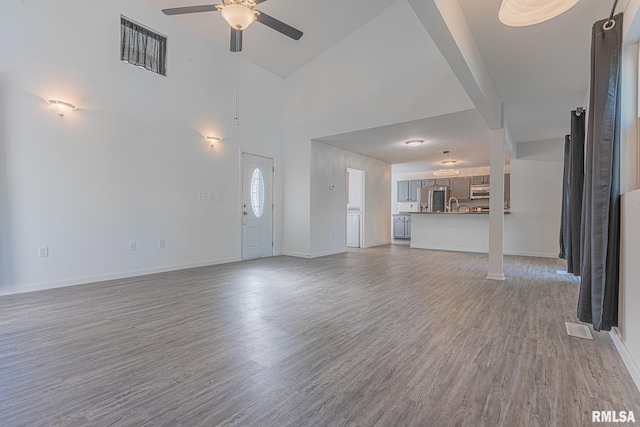 unfurnished living room with hardwood / wood-style floors, ceiling fan, and high vaulted ceiling