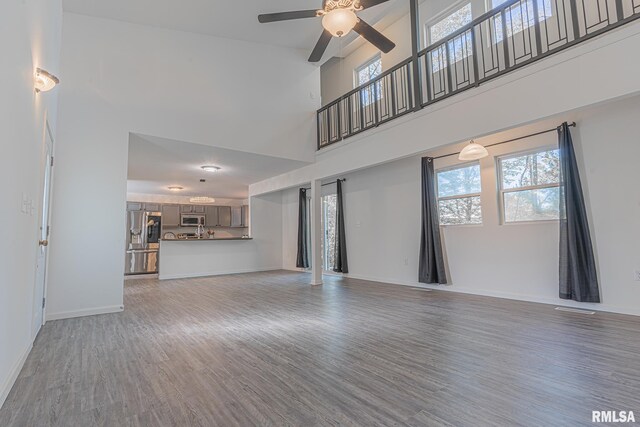 unfurnished living room with hardwood / wood-style flooring, ceiling fan, and a high ceiling