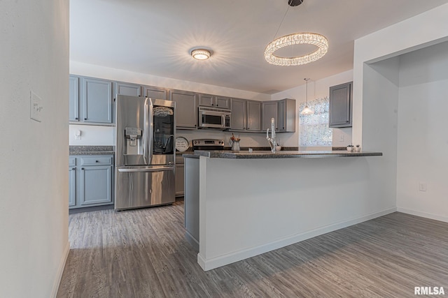 kitchen with kitchen peninsula, pendant lighting, dark wood-type flooring, and stainless steel appliances