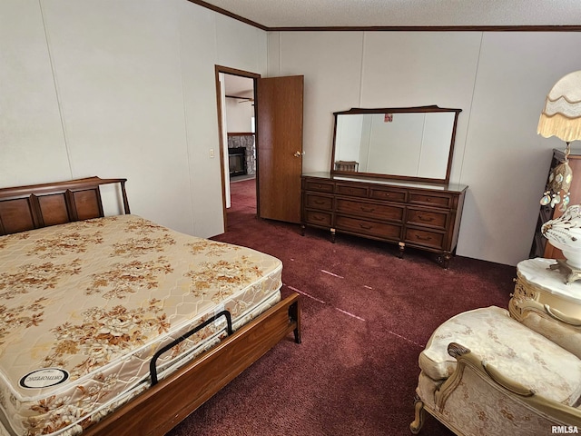 bedroom with dark colored carpet, crown molding, a textured ceiling, and a fireplace