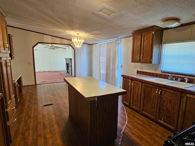 kitchen with ceiling fan with notable chandelier, a textured ceiling, sink, dark hardwood / wood-style flooring, and a center island