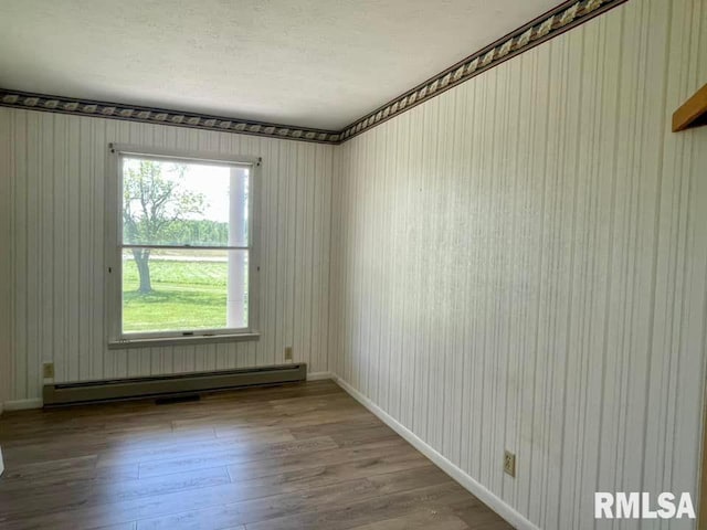 spare room with wood-type flooring, a baseboard radiator, and plenty of natural light