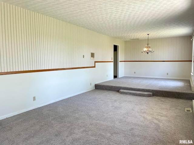 empty room with an inviting chandelier, a textured ceiling, and carpet floors