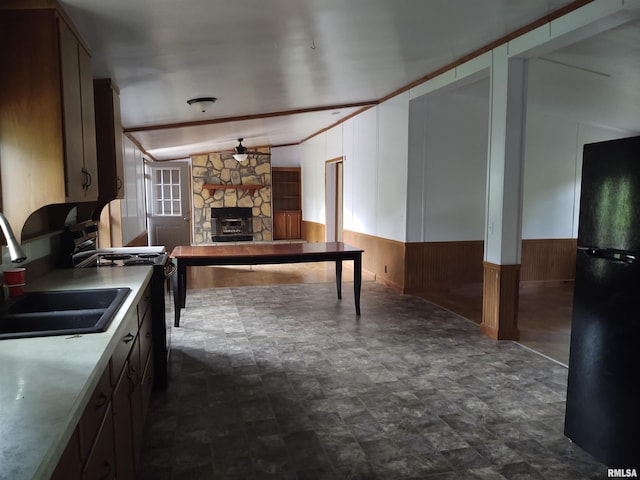 kitchen featuring black appliances, a stone fireplace, sink, wood walls, and ceiling fan