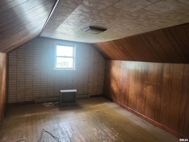 bonus room with wood-type flooring, vaulted ceiling, a baseboard heating unit, and wooden walls