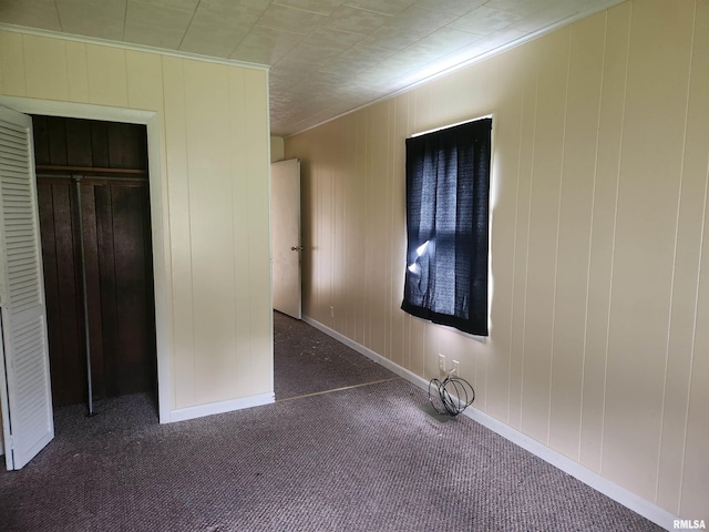 unfurnished bedroom featuring dark carpet, a closet, and wooden walls