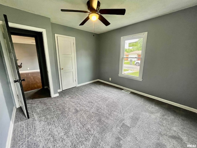 unfurnished bedroom with ceiling fan and dark colored carpet