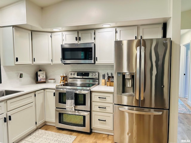 kitchen with appliances with stainless steel finishes, light hardwood / wood-style floors, and tasteful backsplash