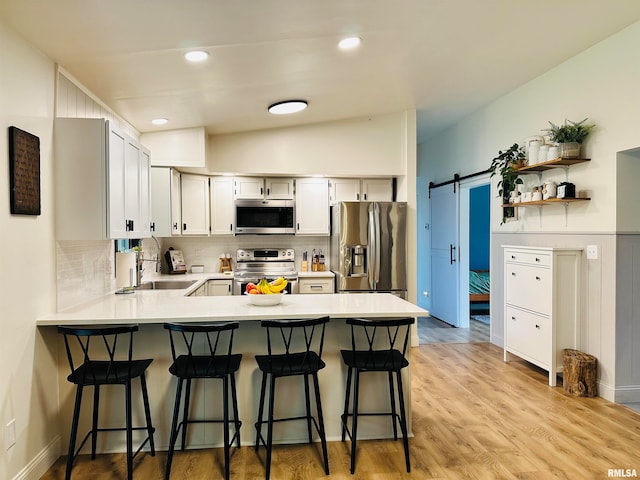 kitchen featuring light hardwood / wood-style flooring, kitchen peninsula, stainless steel appliances, a barn door, and lofted ceiling