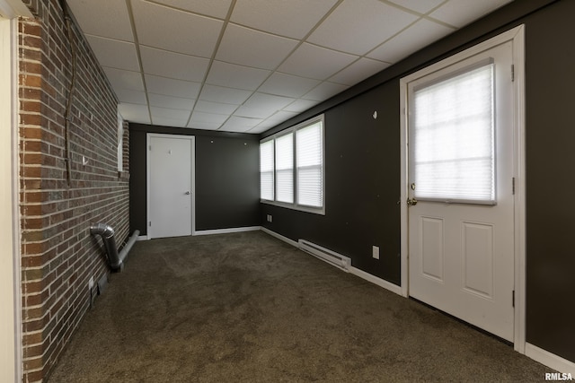 foyer entrance with brick wall, a drop ceiling, dark carpet, and a baseboard heating unit