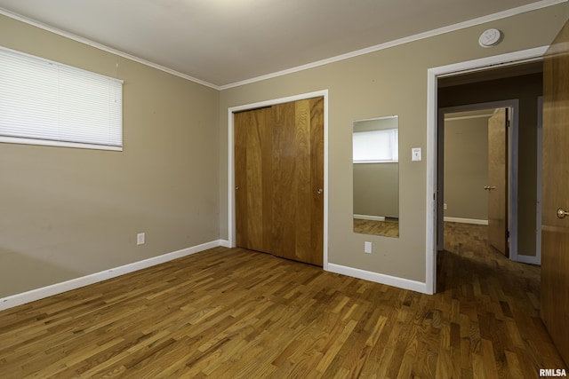 unfurnished bedroom featuring crown molding, multiple windows, hardwood / wood-style floors, and a closet