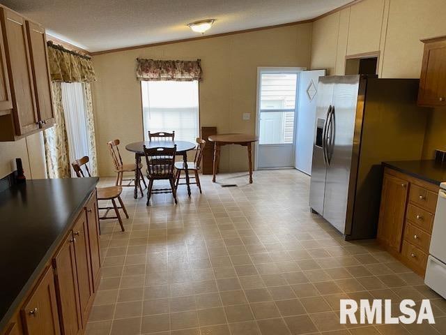 kitchen featuring stainless steel refrigerator with ice dispenser, crown molding, light tile floors, and lofted ceiling