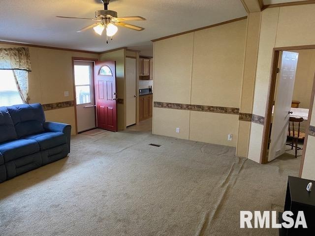 carpeted living room with crown molding and ceiling fan