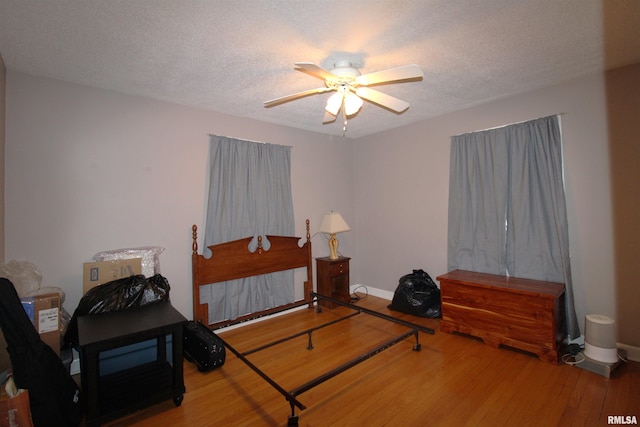 bedroom with ceiling fan, a textured ceiling, baseboards, and wood finished floors