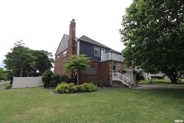 view of property exterior with a balcony, brick siding, fence, and a yard