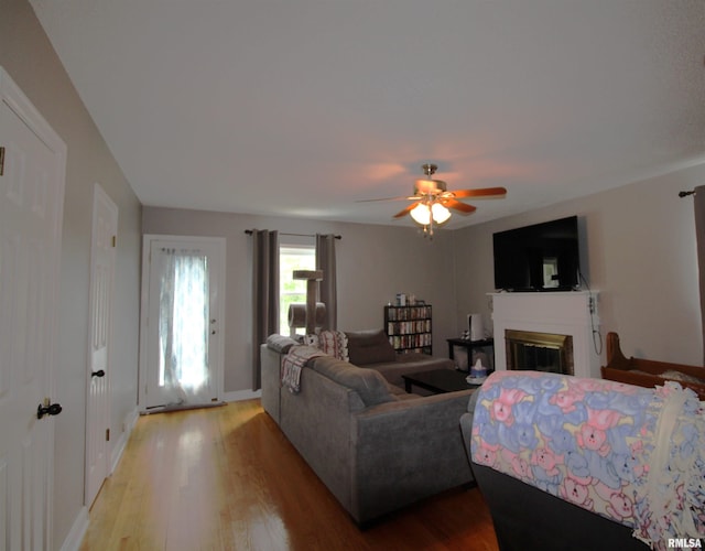 living room featuring light wood-style floors, a glass covered fireplace, ceiling fan, and baseboards