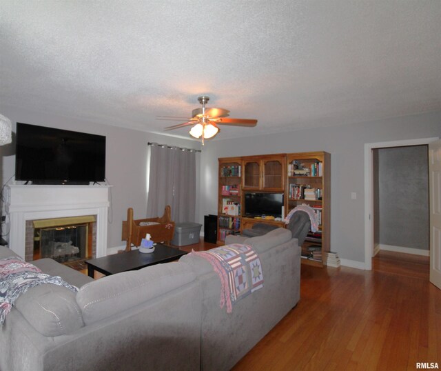 living room with a ceiling fan, a glass covered fireplace, a textured ceiling, wood finished floors, and baseboards