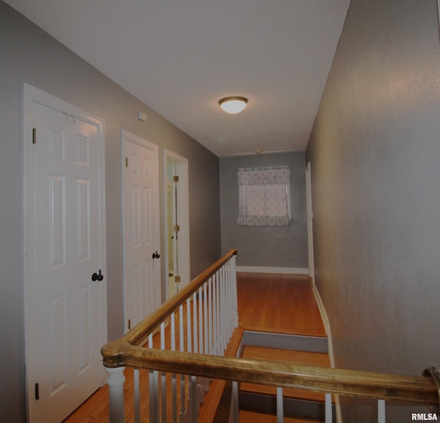 hall with baseboards, wood finished floors, and an upstairs landing