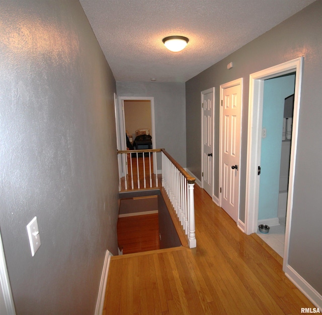 hallway featuring a textured ceiling, light wood-type flooring, an upstairs landing, and baseboards