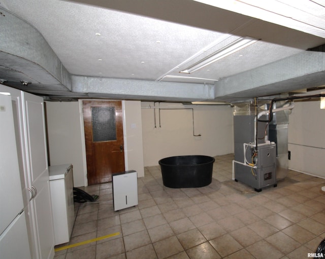 finished below grade area featuring heating unit, freestanding refrigerator, and refrigerator