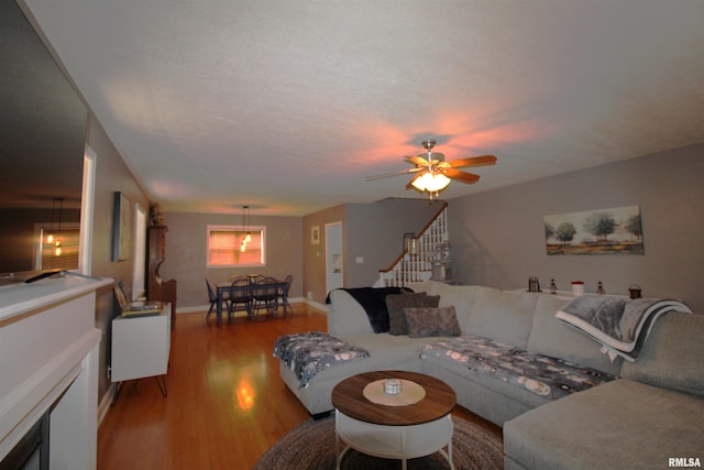 living area with a ceiling fan, stairs, baseboards, and wood finished floors