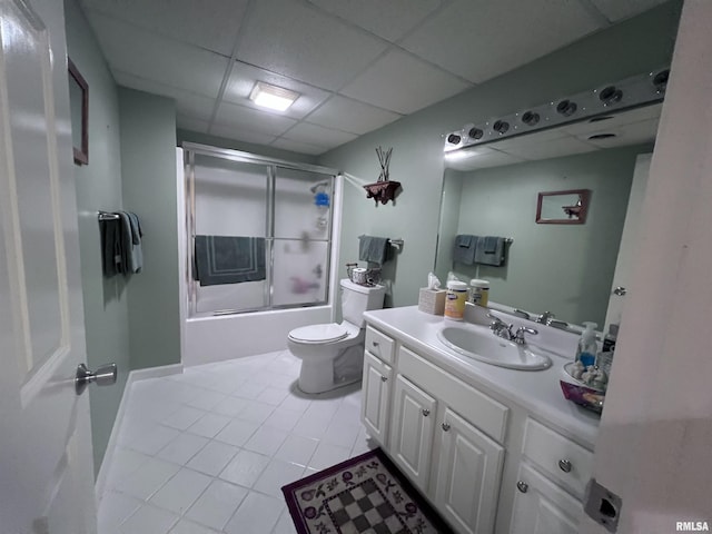 full bathroom with a paneled ceiling, vanity, bath / shower combo with glass door, tile patterned flooring, and toilet