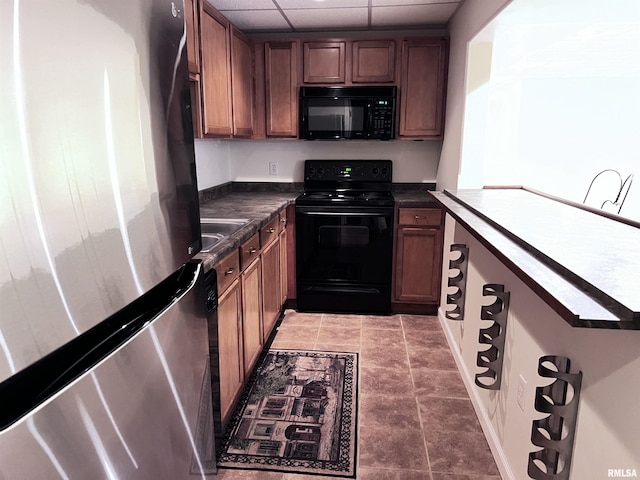 kitchen with tile patterned floors, a drop ceiling, black appliances, and sink