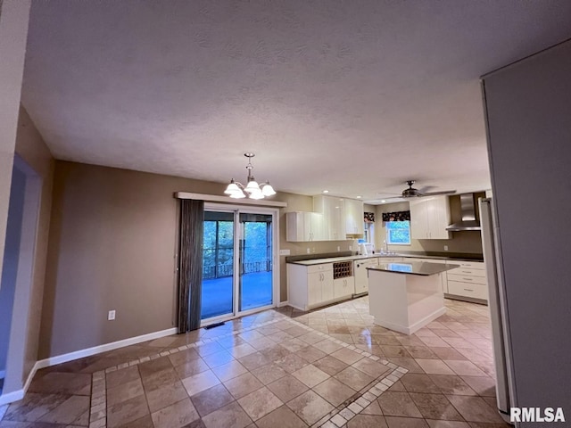 kitchen featuring white cabinetry, wall chimney range hood, kitchen peninsula, pendant lighting, and ceiling fan with notable chandelier