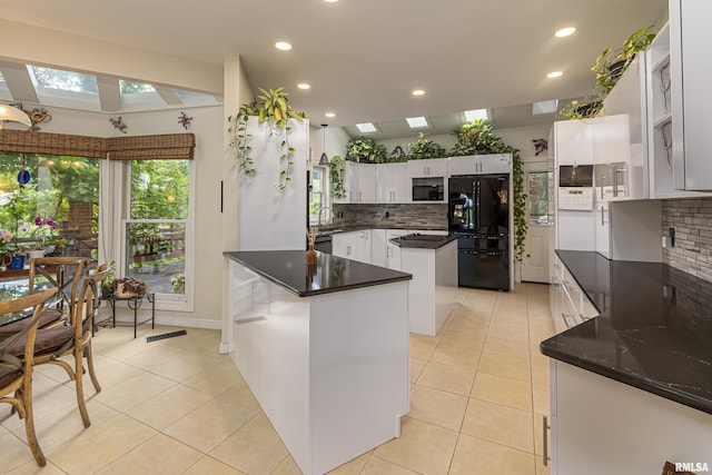 kitchen with a skylight, black fridge, tasteful backsplash, white cabinets, and a kitchen island