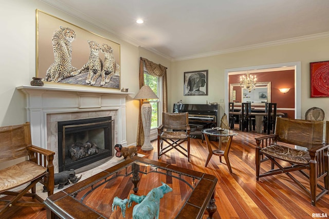 living room featuring a tile fireplace, ornamental molding, wood-type flooring, and a notable chandelier