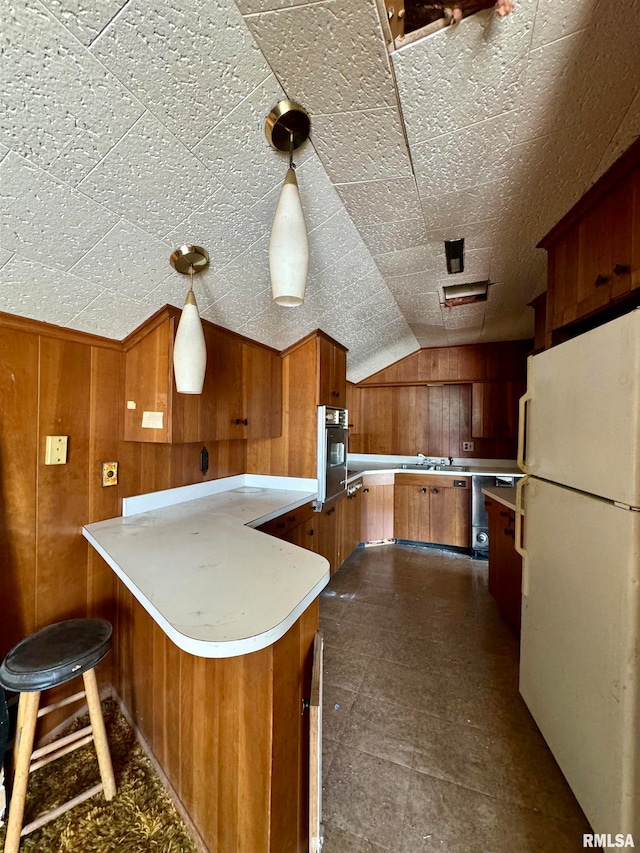 kitchen featuring wooden walls, decorative light fixtures, white refrigerator, and lofted ceiling