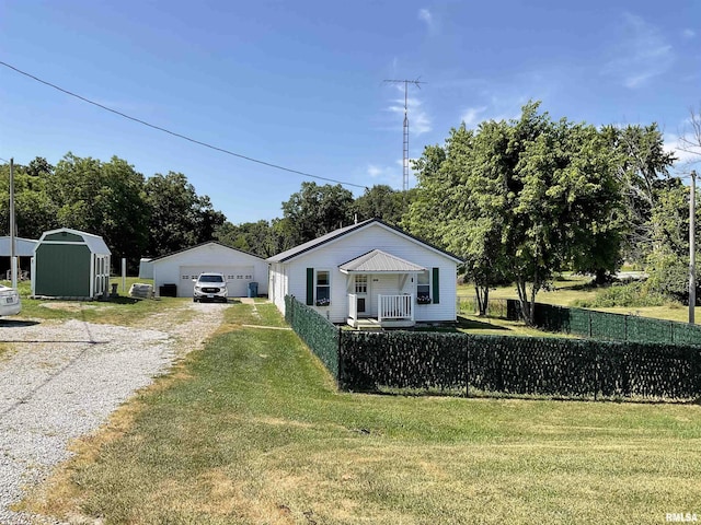 view of front of home featuring a storage shed, covered porch, a front yard, and a garage