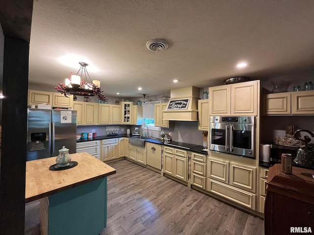 kitchen with sink, butcher block countertops, custom exhaust hood, appliances with stainless steel finishes, and hardwood / wood-style floors