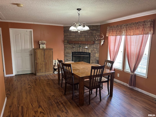 dining room with a textured ceiling, dark wood-type flooring, crown molding, an inviting chandelier, and a stone fireplace