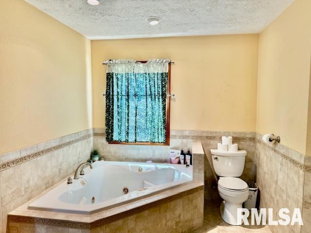 bathroom with tiled tub, toilet, a textured ceiling, and tile walls