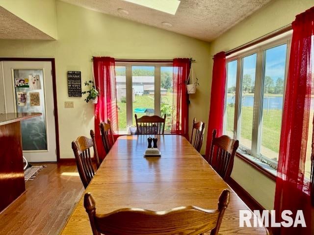 dining space featuring a textured ceiling, a water view, wood-type flooring, and vaulted ceiling