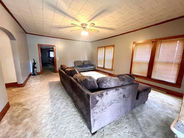 living area featuring arched walkways, ceiling fan, light carpet, baseboards, and ornamental molding