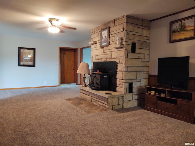 living room featuring ceiling fan, a stone fireplace, carpet floors, and a wood stove