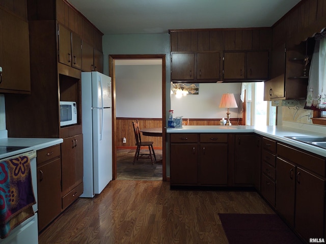 kitchen featuring dark brown cabinetry, wood walls, dark wood-type flooring, and white appliances