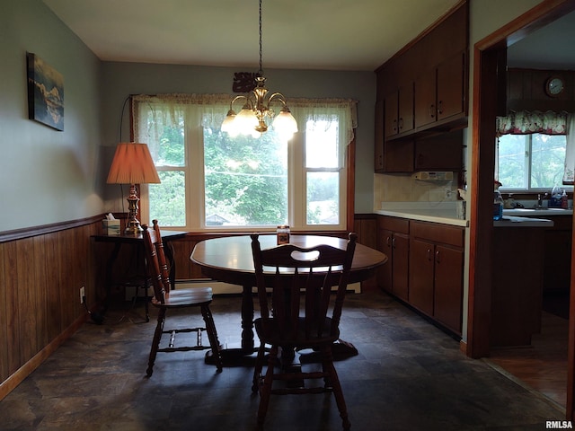 dining room featuring an inviting chandelier, wooden walls, and a wealth of natural light