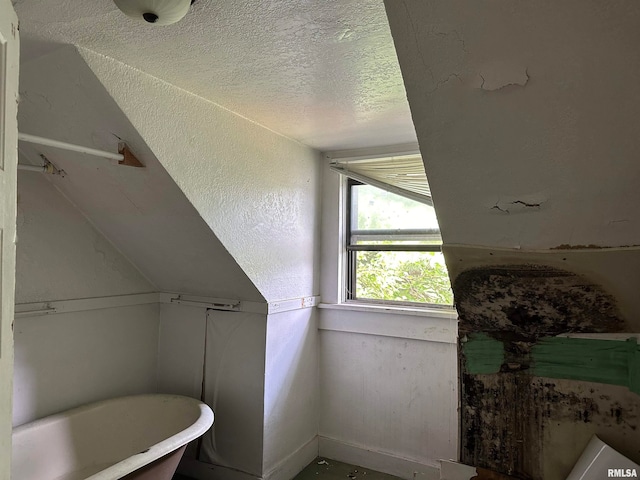 bathroom featuring vaulted ceiling, a bath, and a textured ceiling