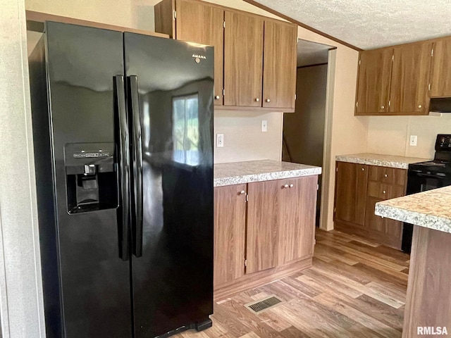 kitchen with light hardwood / wood-style floors, vaulted ceiling, a textured ceiling, black appliances, and exhaust hood