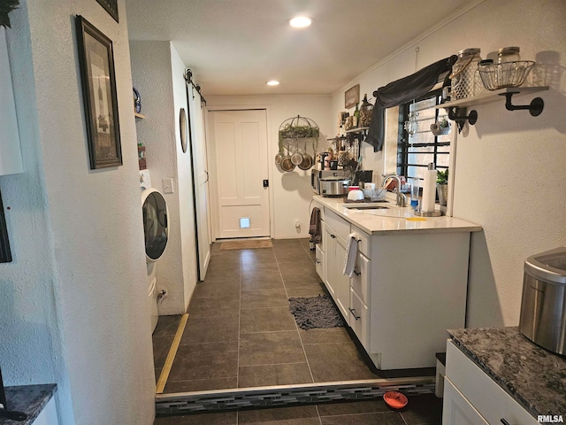 kitchen with washer / dryer, a barn door, white cabinets, ornamental molding, and sink