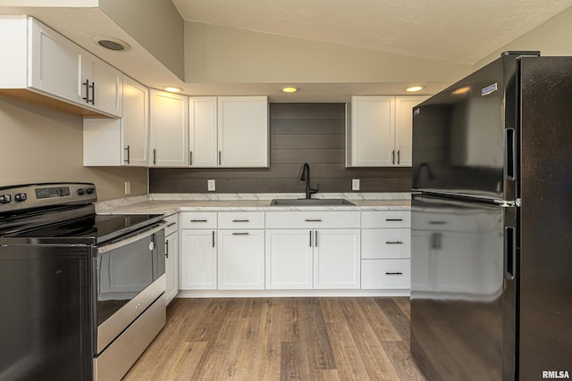 kitchen featuring black refrigerator, stainless steel range with electric stovetop, sink, and white cabinets