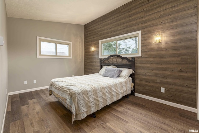 bedroom featuring multiple windows, dark wood-type flooring, and wood walls