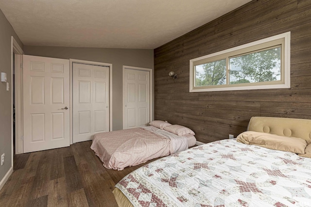 bedroom with vaulted ceiling, dark hardwood / wood-style floors, multiple closets, and wood walls